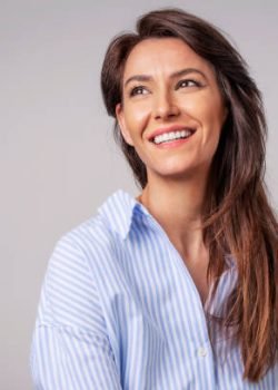Smiling brunette businesswoman sitting against gray background. Confident female professional is wearing blue shirt. She is having brown hair. Copy space.